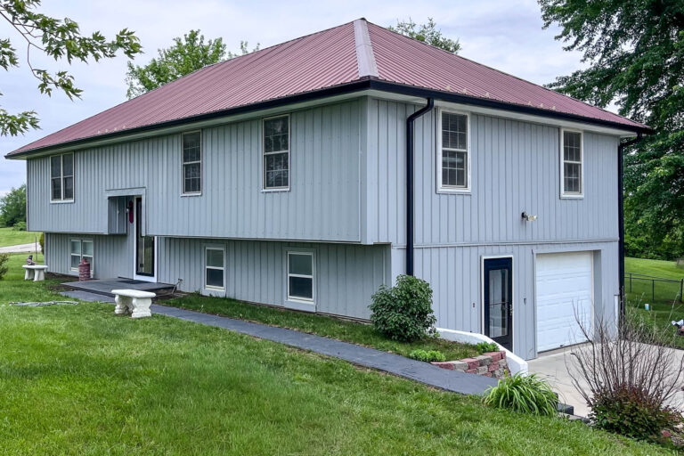 Residential home in Rayville, MO with new 6-inch black seamless gutters installed to manage runoff from a red metal roof.