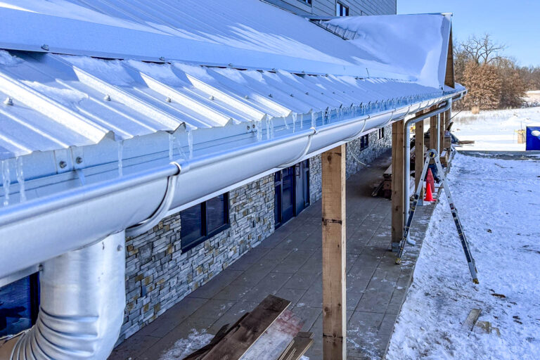 Galvanized half-round gutter system installed along a snowy metal roofline in Polo, Missouri.