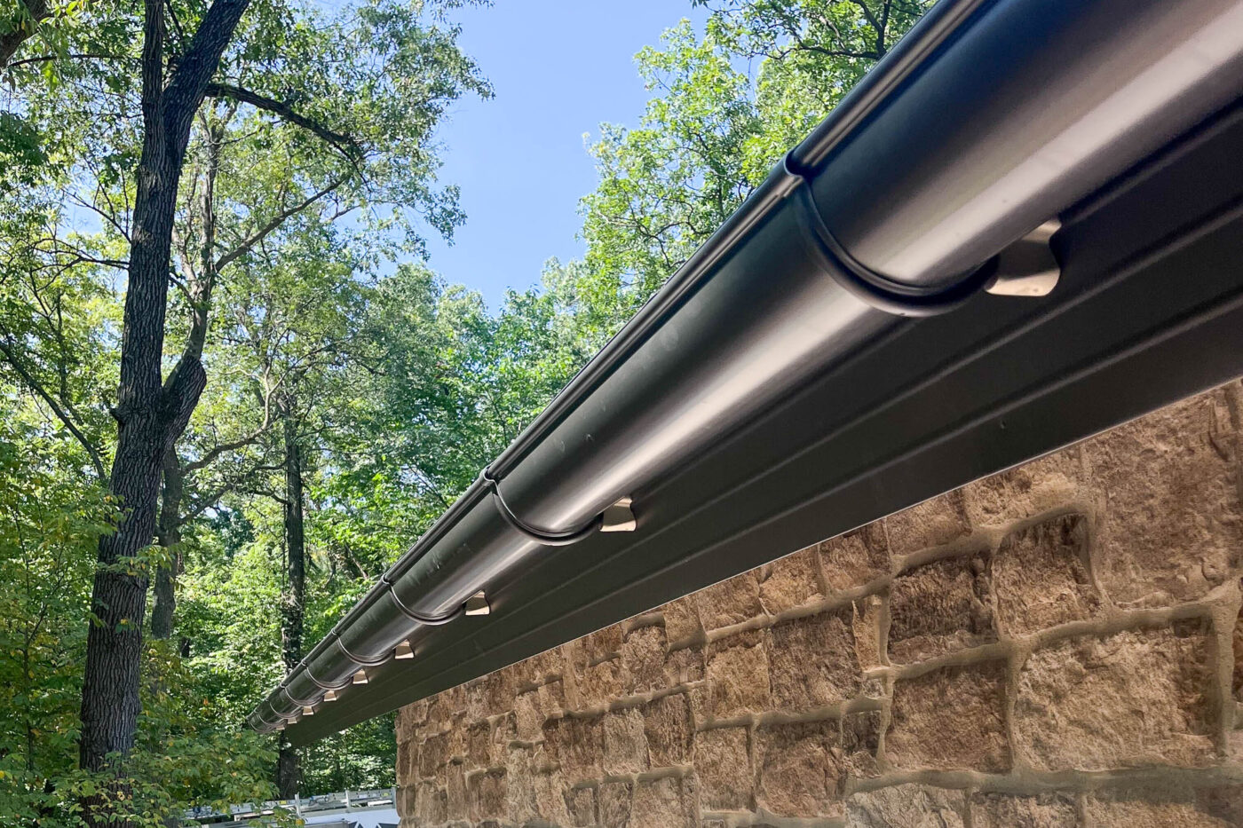 Close-up of bronze half-round gutter with leaf guard installed on a stone wall.