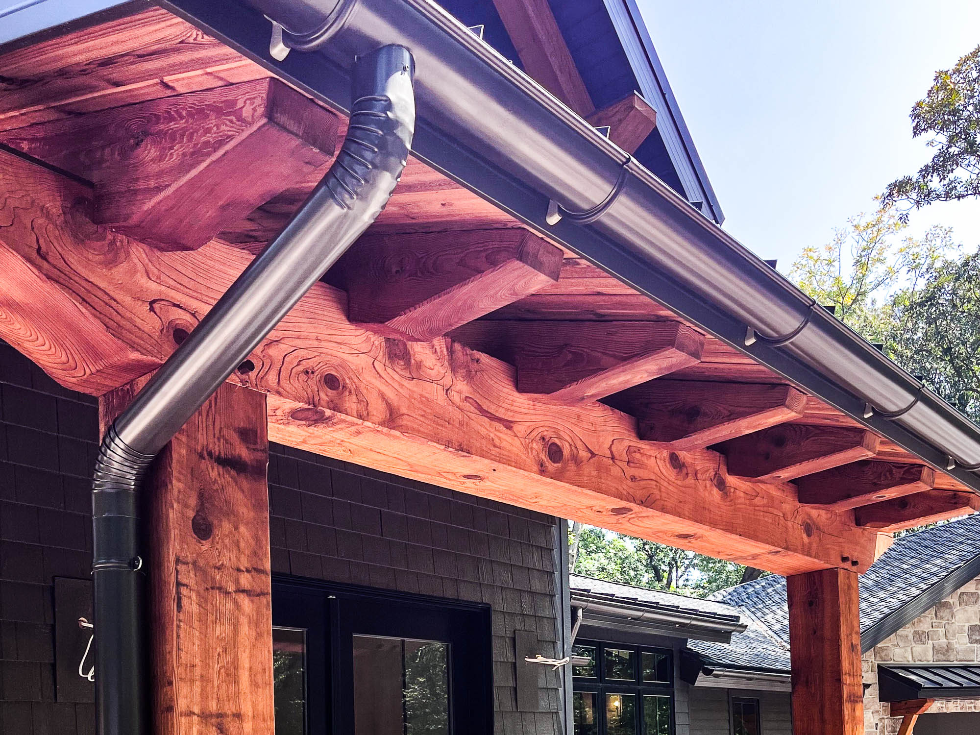 Entryway view showing bronze half-round gutter and downspout complementing wood beams.