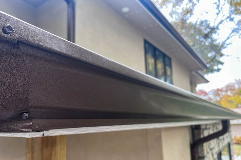 Close-up view of a copper-aluminum downspout installed on a stucco exterior wall in Leawood, Kansas.