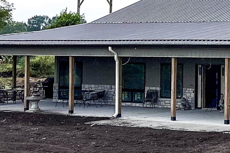 Close-up of black downspout on metal-roof building showing new gutter installation.