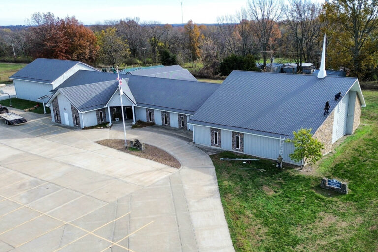 Angled aerial view of a church showing clean gutter lines installed along the roof edges, with surrounding autumn trees and well-maintained grounds.