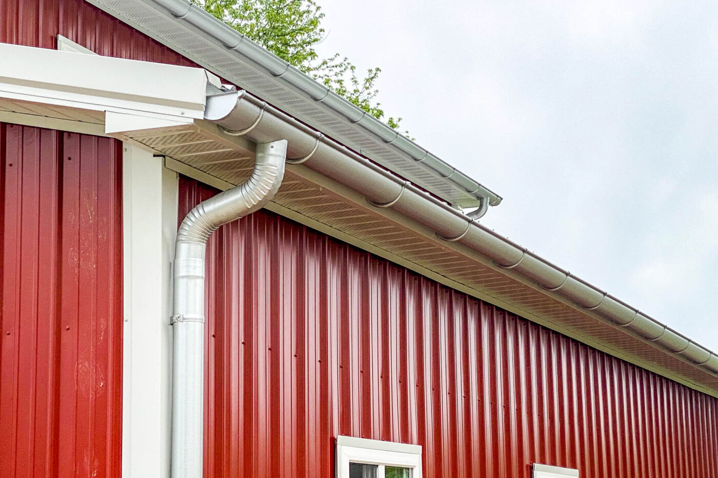 Angled view of galvanized half-round gutters and downspouts installed on a red metal building in Rosebud, Missouri.