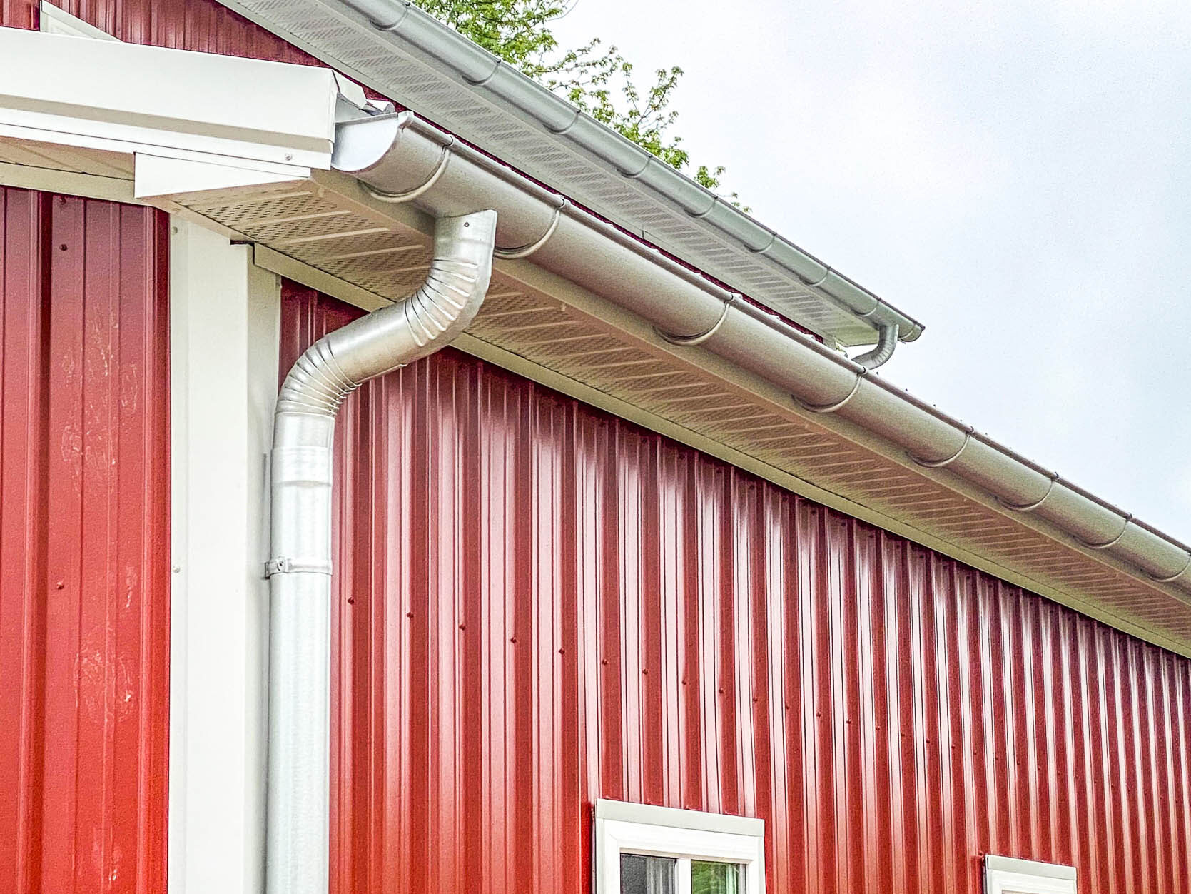 Side view of a red metal building with new 6-inch galvanized gutters and round downspouts.