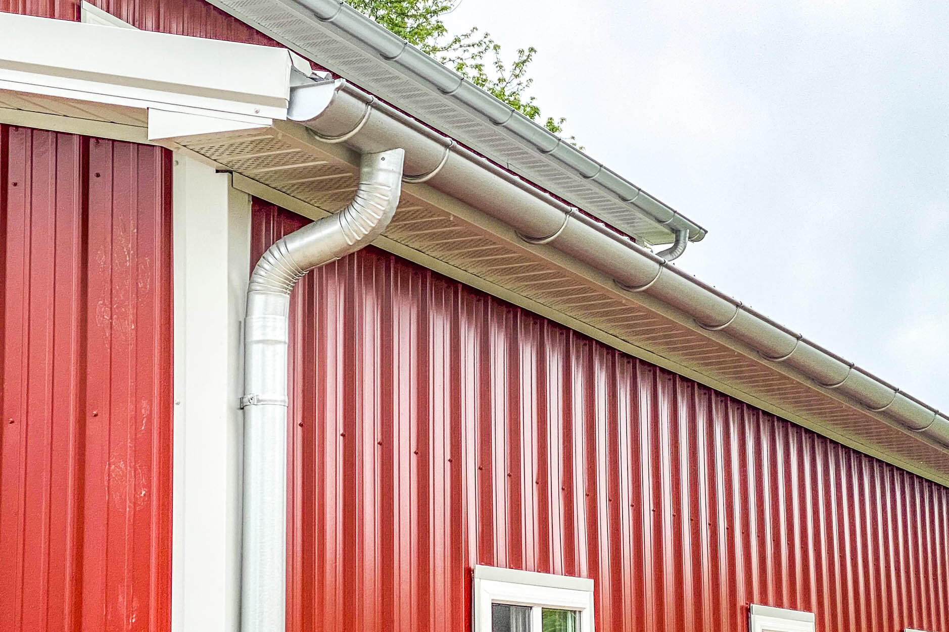 Side view of a red metal building with new 6-inch galvanized gutters and round downspouts.