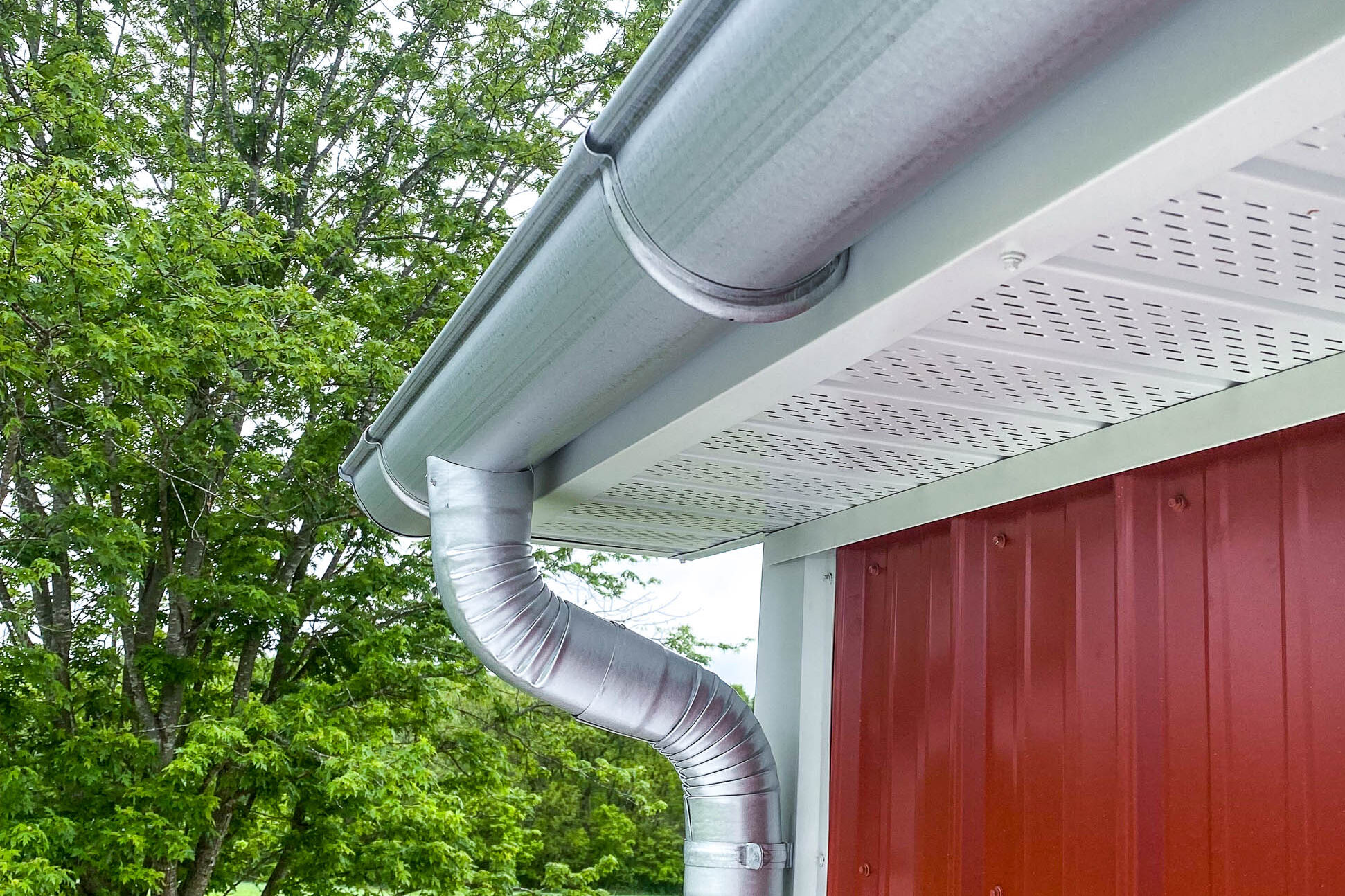 Close-up of a galvanized half-round gutter and round downspout installed on a red metal building in Rosebud, Missouri.