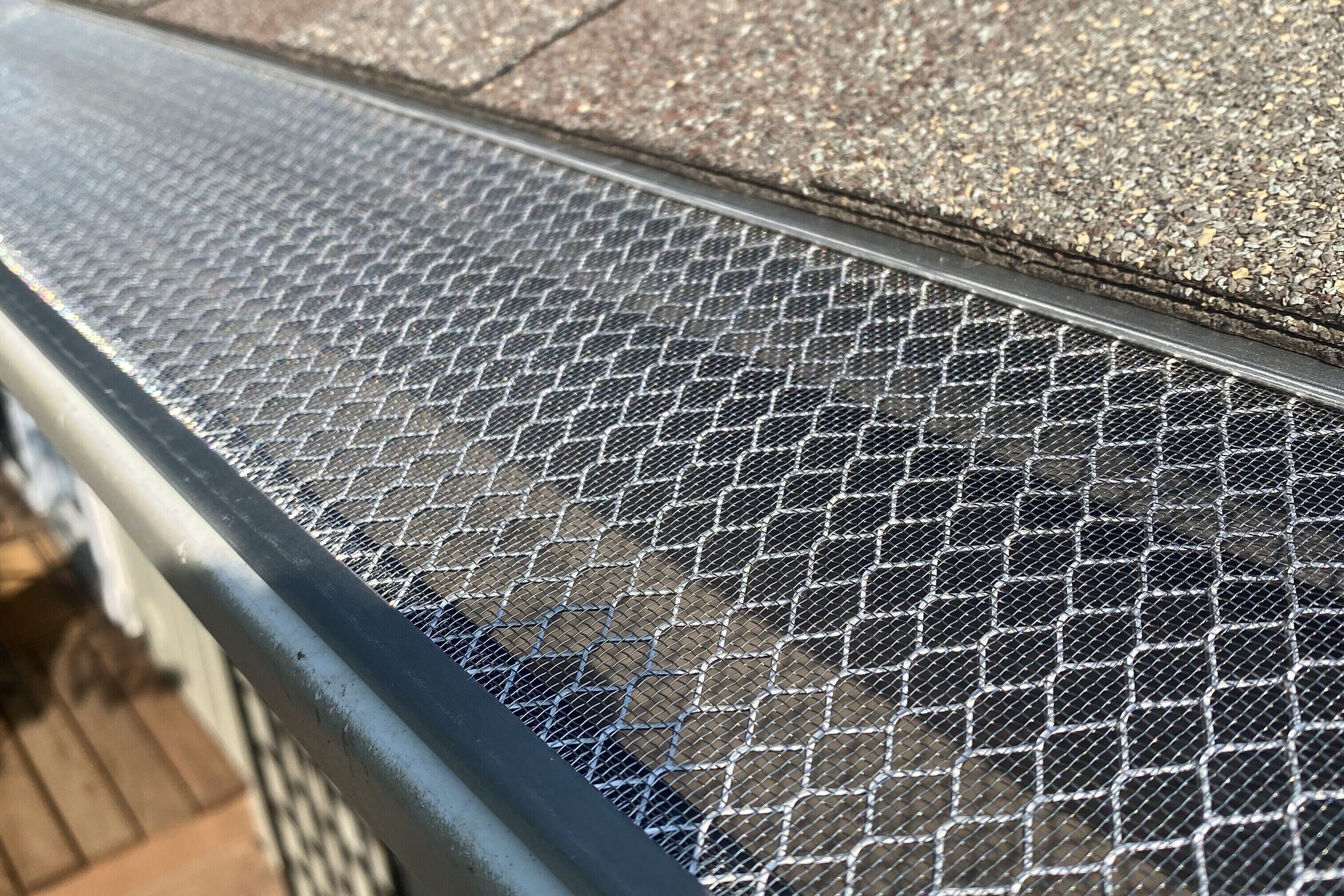 Close-up of an Xtreme Leaf Guard with stainless steel mesh installed on a residential gutter, positioned beneath asphalt roof shingles.
