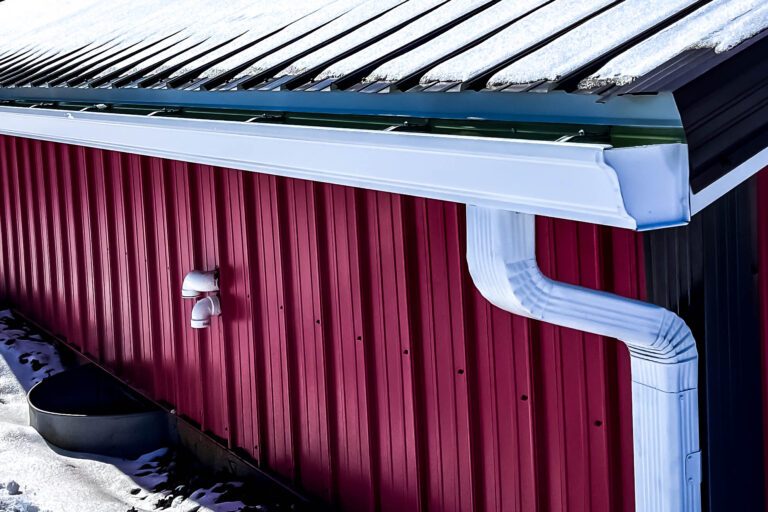 White aluminum gutter system installed on a red metal building with a downspout.