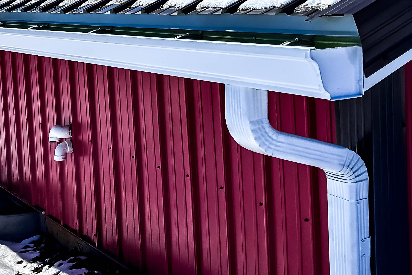 White aluminum gutter system installed on a red metal building with a downspout.